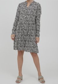 Pitkähihainen mustavalkoinen kuvioitu mekko, jossa on V-pääntie ja rypytetty vyötärö, teksturoitu kangas, yhdistetty harmaiden tupsukorolla varustettujen korkokenkien kanssa.