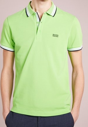 Mand iført limegrøn Hugo Boss polo med hvide og sorte striber på kraven og ærmekanter, kombineret med mørke bukser.