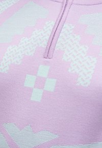 Gros plan sur un vêtement tricoté violet clair avec des motifs géométriques croix et zigzag vert pâle et une courte fermeture éclair verticale près du col.
