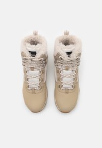 Beige fotturstøvler med faux pelskrage, teksturerte hvite paneler, metalløye, og runde snører med et mønster.