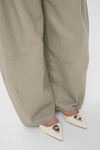 Μπεζ παντελόνια με ευρύ μήκος που καλύπτουν τους αστραγάλους, φορεμένα με κρεμ παπούτσια μυτερά, διακοσμημένα με μεγάλα μεταλλικά στολίδια σε σχήμα καρδιάς.