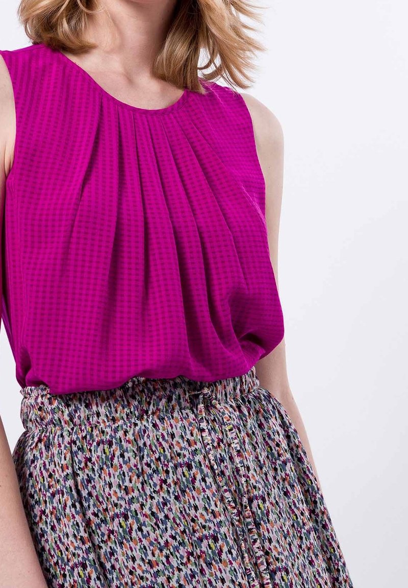 Donna che indossa un top magenta senza maniche con plissettature abbinato a una gonna alta in vita multicolore con vita regolabile.