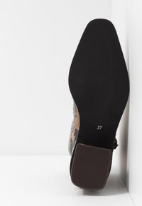 Suela de una bota de tobillo para mujer con tacón cuadrado y parte superior de estampado de serpiente, mostrando el tamaño 37 en la suela negra.