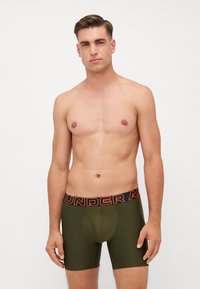 Men's olive green boxer briefs with a black waistband featuring orange "UNDER ARMOUR" text, offering a fitted design and smooth texture.