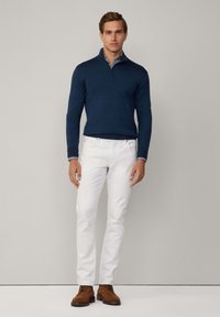 Meerblauer Halbpullover, weiße Slim-Fit-Jeans und braune Schnürschuhe, mit einem Karomuster am Hemdkragen.
