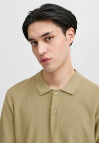 Khaki polo tričko s texturovaným pletením, s límečkem a dvěma knoflíkovými zapínáními. Střih je pohodlný a jednoduchý.