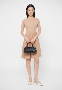 Vestido em bege com mangas curtas, saia rodada, e uma bolsa preta com duas alças. Sapatos planos brancos com bico fino completam o visual.