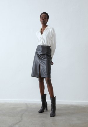 Blusa bianca a colletto abbinata a una gonna nera in pelle lunga fino al ginocchio con uno spacco frontale, completata da stivaletti neri con tacco a blocco.