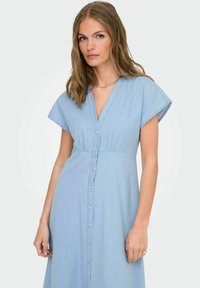Ljust blå denimklänning med v-ringning, korta ärmar med cap-sleeve, knapprad fram och resår i midjan för en avslappnad passform.