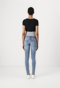 Top corto negro de canalé ajustado con mangas cortas, combinado con unos jeans ajustados de cintura alta en azul claro con dobladillo desflecado, calzando zapatillas blancas.