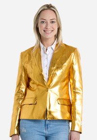 Blazer metálico dorado con un diseño ajustado, solapas de muesca, dos bolsillos frontales y cierre de un solo botón, usado sobre una camisa blanca.