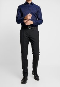 Mörkblå långärmad skjorta med ett vågigt mönster, matchad med svarta skräddarsydda byxor och svarta snörskor, komplett med ett svart bälte.