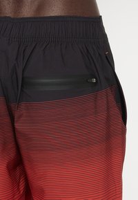 Costumi da bagno a strisce nere e rosse con elastico in vita, dotati di una tasca con zip sul lato e realizzati in tessuto leggero e liscio.