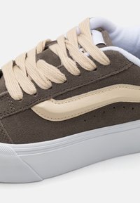 Brown suede sneaker with beige accents, thick beige laces, and white rubber sole. Features a classic design and subtle perforations on the side.