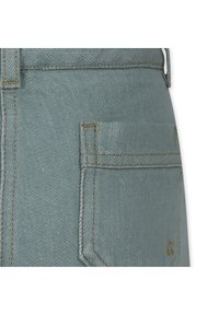 Jasnoniebieskie dżinsy z materiału z tylną kieszenią z żółtym przeszyciem. Tkanina ma teksturowany wygląd i standardowy krój.