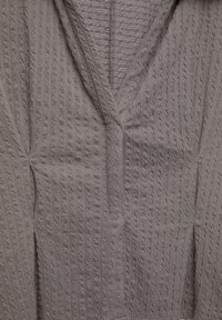 Grauer strukturierter Cardigan mit V-Ausschnitt, geripptem Muster und weichem Stoff. Geschmeidige Oberfläche mit sichtbaren Nähten und überlappenden Frontkanten.