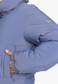 Lichte blauwe pufferjack, voorzien van een capuchon, elastische manchetten, zijzakken en een logo-opdruk op de mouw. Soepele, geïsoleerde materiaal.