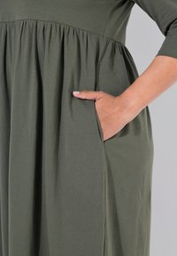 Olivegrön klänning i mjukt tyg, med resårmidja och sneda sidofickor. Trekvartsärmar och avslappnad passform.