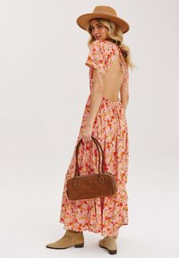 Kvetinové maxi šaty v ružových a oranžových odtieňoch, s krátkymi rukávmi a odhalenými chrbátom. V kombinácii s hnedou kabelkou a béžovými členkovými čižmami.