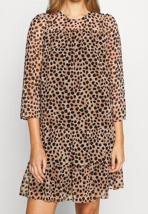 Kvinde iført en knælængde, langærmet kjole med en lys brun base og uregelmæssigt sort leopardmønster.