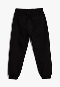 Zwarte sweatpants met een elastische tailleband, gathered manchetten en twee achterzakken. Gemaakt van een gladde stof met een matte afwerking.