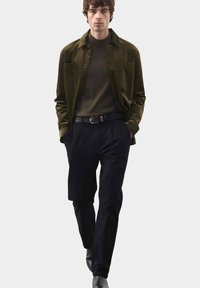 Ciemnozielona koszula kordowa na ciemnooliwkowym golfie, zestawiona z dopasowanymi czarnymi spodniami i czarnym paskiem. Gładkie faktury, dopasowany krój.