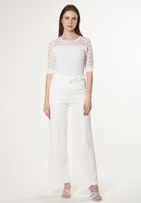 Weißes, geripptes Oberteil mit durchsichtigen gestreiften Ärmeln, kombiniert mit weißen, weit geschnittenen Hosen mit einem gegurteten Taillenbund. Glatte Textur und taillierter Schnitt.