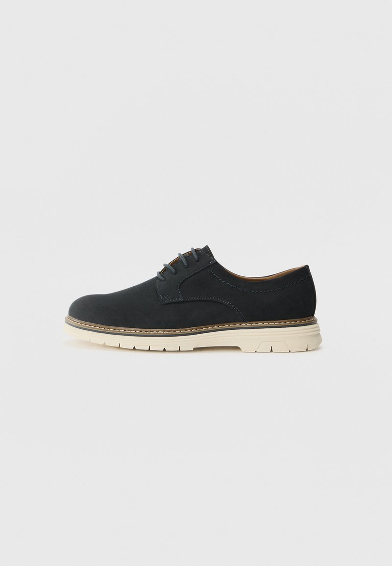 Schwarze Wildleder-Oxfordschuhe mit runder Zehenform, beigem Gummisohle und fünf Ösen für Schnürsenkel, die dekorative Nähte entlang der Nähte aufweisen.