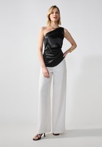 Black satin one-shoulder top with draped design, paired with high-waisted white wide-leg trousers, and black strappy heels. Gold jewelry accents.