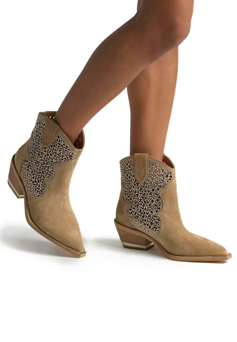 Botas de tobillo de ante marrón con diseño con volantes y adornadas con tachuelas de plata. Presentan una puntera afilada y un tacón apilado.