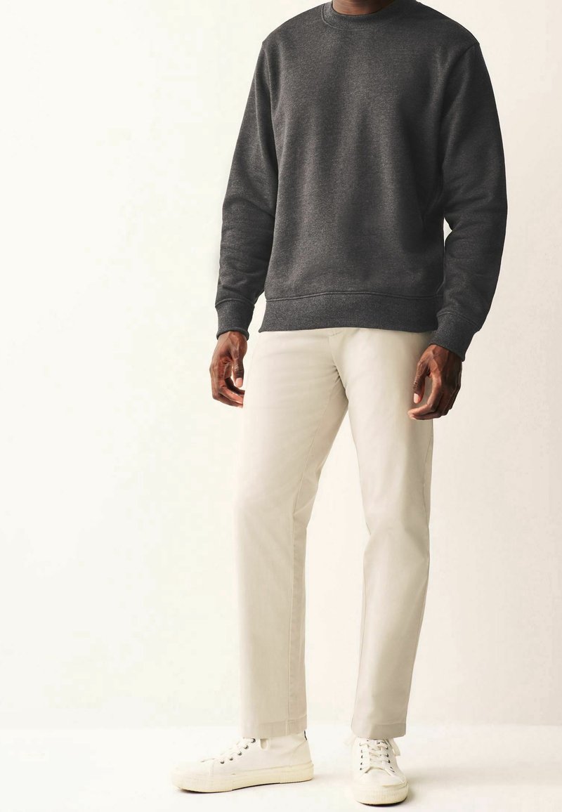 Šedá mikina s vroubkovanými manžetami v kombinaci s krémovými kalhotami a bílými teniskami. Tkanina se zdá být měkká s hladkým povrchem.