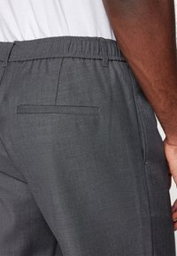 Sive hlače od glatkog materijala s elastičnom jaknom, s jednim stražnjim džepom i krojem koji naglašava elegantnu siluetu.