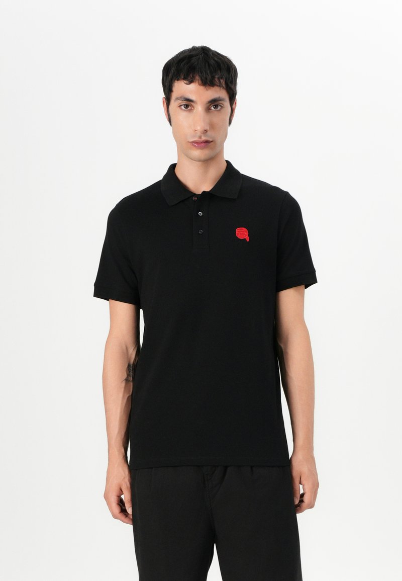 Μαύρο πόλο μπλουζάκι από βαμβάκι με κοντό μανίκι, γιακά, πλάγιο κλείσιμο με τρία κουμπιά και κόκκινο κεντημένο λογότυπο στην αριστερή θήκη του στήθους.