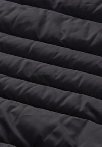 Černá izolační látka s horizontálními prošívanými vzory a hladkou texturou. Povrch působí měkce s minimálním leskem.