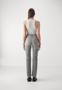 Jeans grises de talle alto con un diseño de pierna recta, que cuentan con bolsillos traseros y un sutil acabado texturizado, combinados con una camiseta sin mangas blanca.