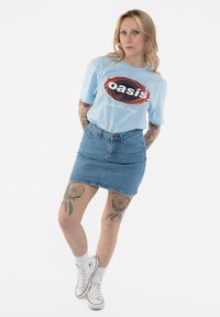Light blue short-sleeve t-shirt with black and red "oasis" graphic. Paired with a denim mini skirt featuring vertical stripes. Worn with white sneakers.