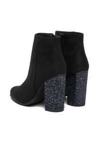 Stivali ankle in suede nera con tacco quadrato glitterato nero. Parte superiore liscia con chiusura a cerniera sul retro, che evidenzia un design strutturato.