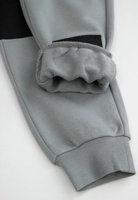 Szare dresy z czarnymi akcentami, z prążkowanym ściągaczem i miękką teksturą. Zbliżenie uwypukla szczegóły ściągacza i kroju.