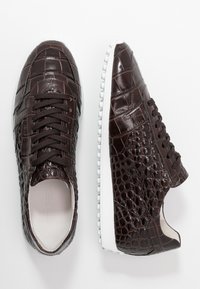 Baskets en cuir à motif crocodile brun avec bout rond, design à lacets, semelle en caoutchouc blanc proéminente et détails de surface texturés.