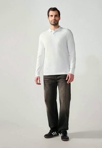 Long-sleeve white polo shirt with a collared neck, paired with dark jeans and black shoes featuring white stripes. Minimalist design, casual fit.