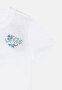 Camiseta blanca de algodón con un colorido logo de Levi's que presenta palmeras y montañas en un diseño circular. Manga corta y cuello redondo.