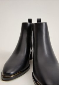 Zwarte leren enkelboots met een puntige neus, een slank ontwerp, gouden accenten bij de basis en trekbanden voor eenvoudig aan- en uittrekken.