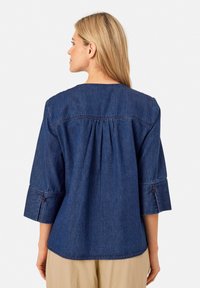 Top in denim con scollatura tonda, maniche a tre quarti e dettagli arricciati sul retro. Caratterizzato da una consistenza morbida e di colore blu navy.