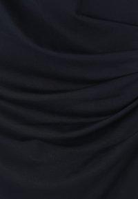 Tumši zils audums ar gludu, mīkstu tekstūru un maigām, plūstošām krokām un locījumiem.