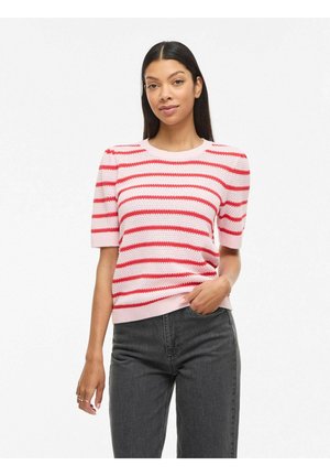 Kvinde iført en kortærmet strikket top med pink og røde striber og pufærmer, kombineret med højttaljede mørkegrå jeans.