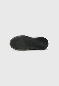 Semelle de chaussure en caoutchouc noir avec une texture ondulée, dotée de rainures et de stries, conçue pour offrir une meilleure adhérence ; forme générale ovale avec un contour légèrement courbé.