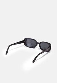 Óculos de sol pretos em plástico, com formato retangular, lentes escuras e braços largos e elegantes com detalhes de marca nas laterais.
