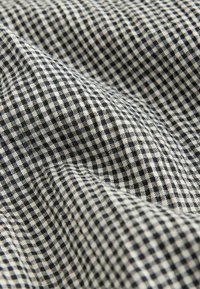 Černá a krémová kostkovaná látka s měkkou, texturovanou vazbou, zobrazující mřížkový vzor malých čtverců.