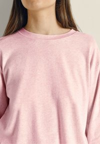 Šviesiai rožinė, ilgarankovė džemperis, pagamintas iš minkštos, tekstūruotos medžiagos; turi plačią iškirptę ir laisvą siluetą, su minimaliu siūlių skaičiumi.