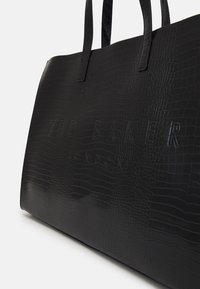 Crna torba od umjetne kože s teksturom krokodila, s urezanim logotipom "TED BAKER" i dvostrukim ručkama.